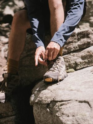 Close-up of a hiker tying boots on a rocky trail, emphasizing outdoor adventure.