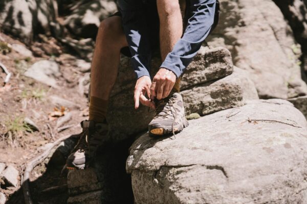 Close-up of a hiker tying boots on a rocky trail, emphasizing outdoor adventure.