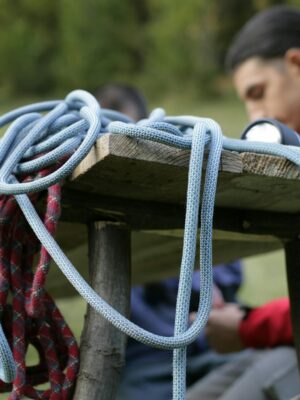 Close-up of climbing ropes on a wooden table with a climber in the background wearing a safety harness.