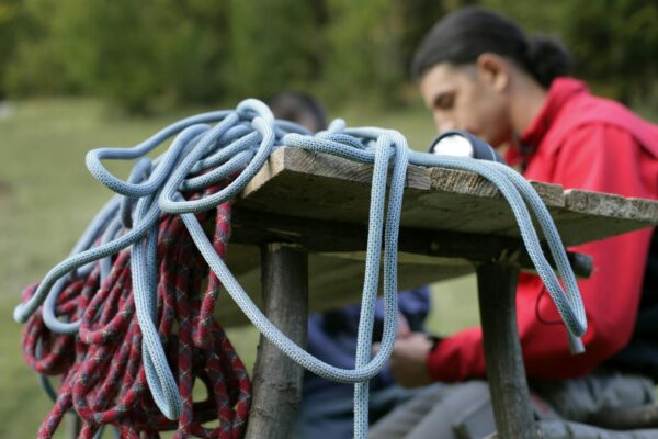Close-up of climbing ropes on a wooden table with a climber in the background wearing a safety harness.